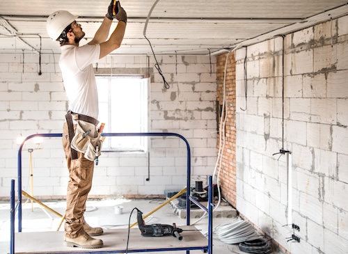 Electrician installer with a tool in his hands, working with cable on the construction site.